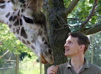 Keeper Brent Huffman and a Giraffe stand side by side 